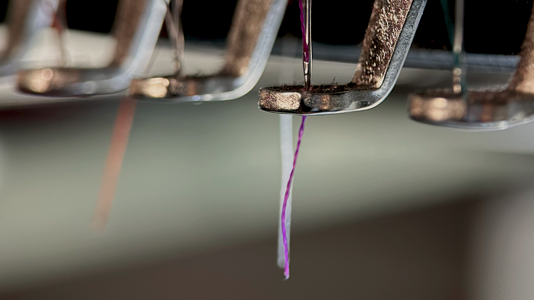 Detailaufnahme einer industriellen Stickmaschine bei MyStitch in Langenthal – Präzise Textilveredelung mit lila Garn.“